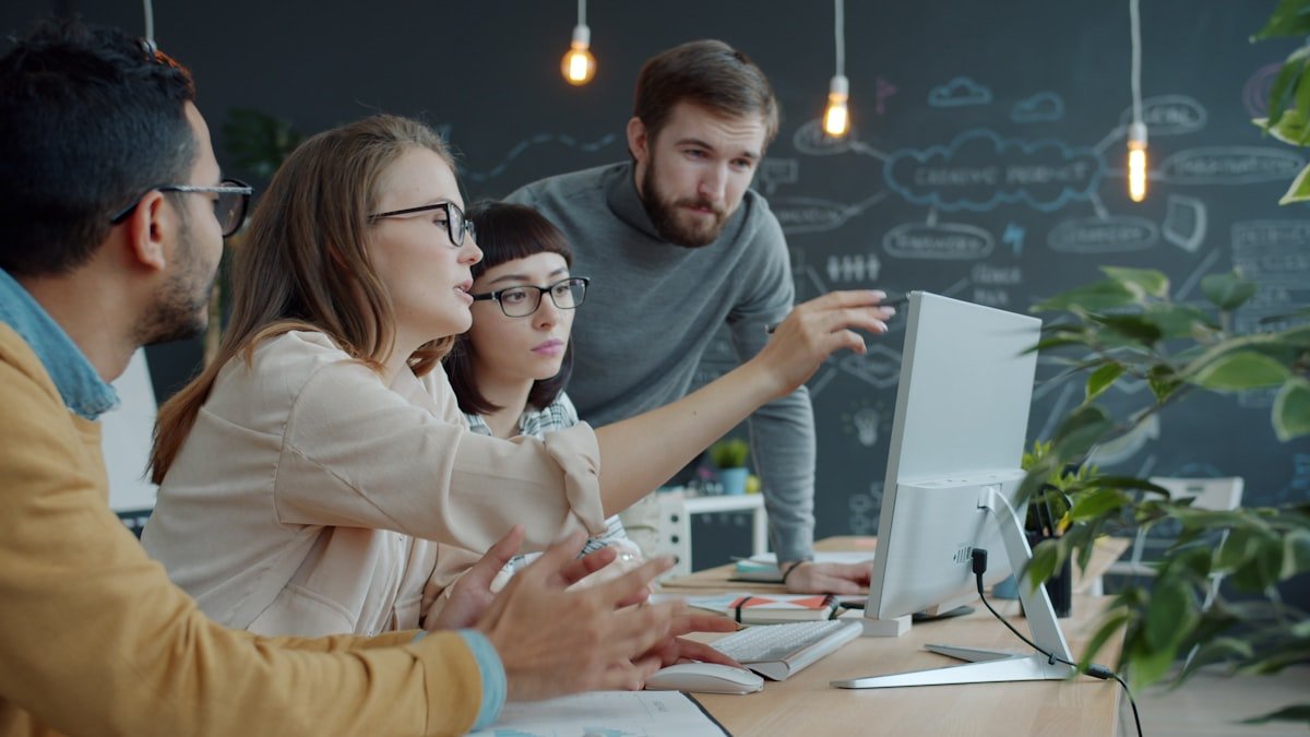 Team collaborating around a computer screen in a creative office workspace.