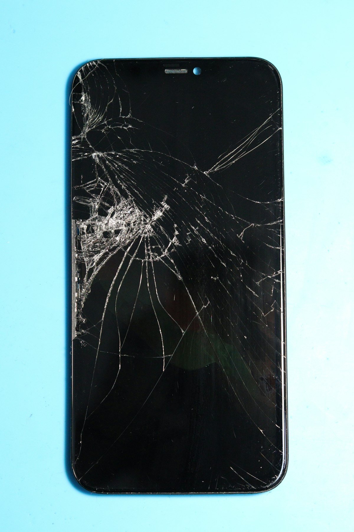 Cracked smartphone screen on a blue surface ready for repair service.