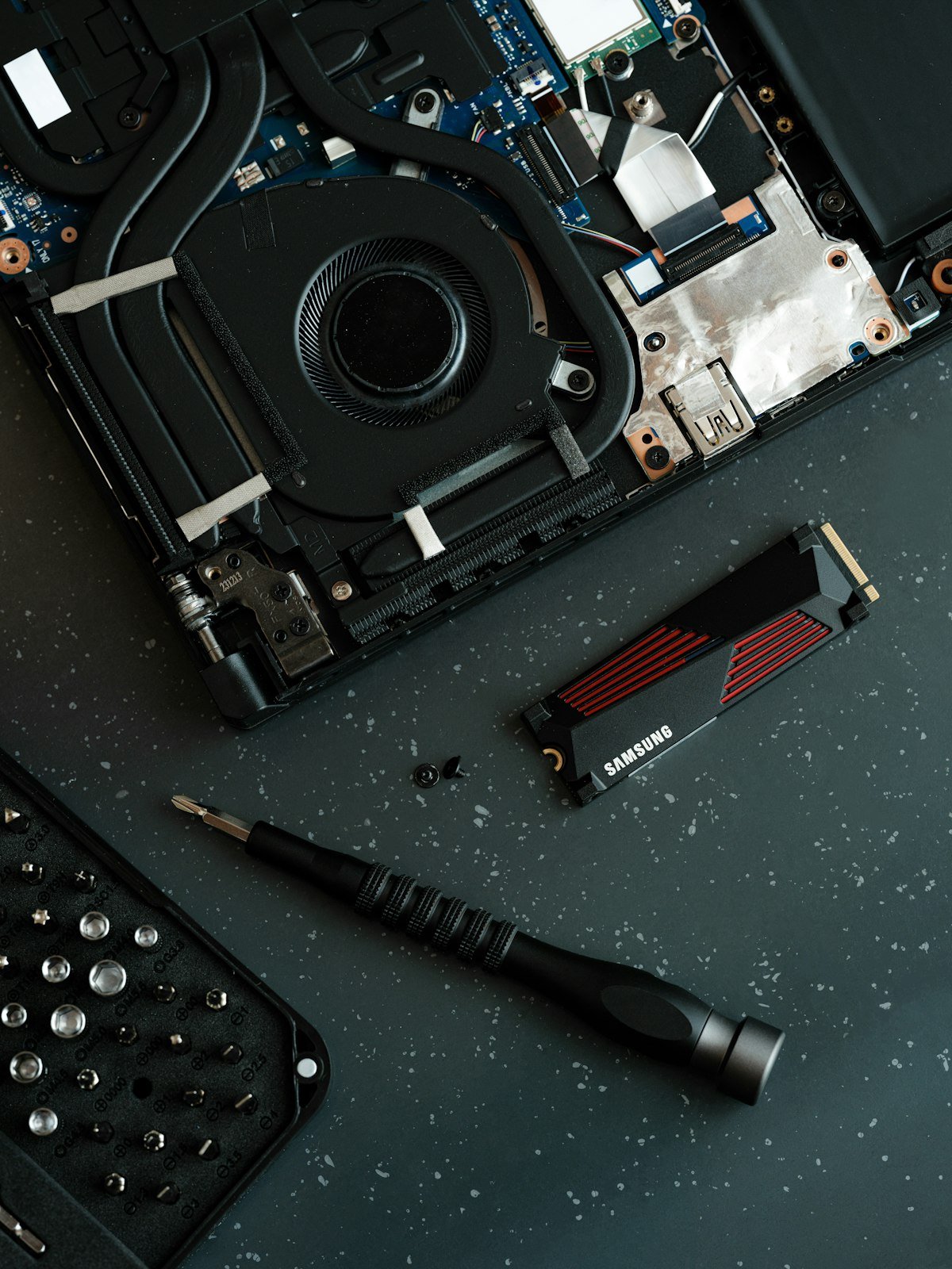 Disassembled laptop with SSD, precision screwdriver, and repair tools on a workbench.