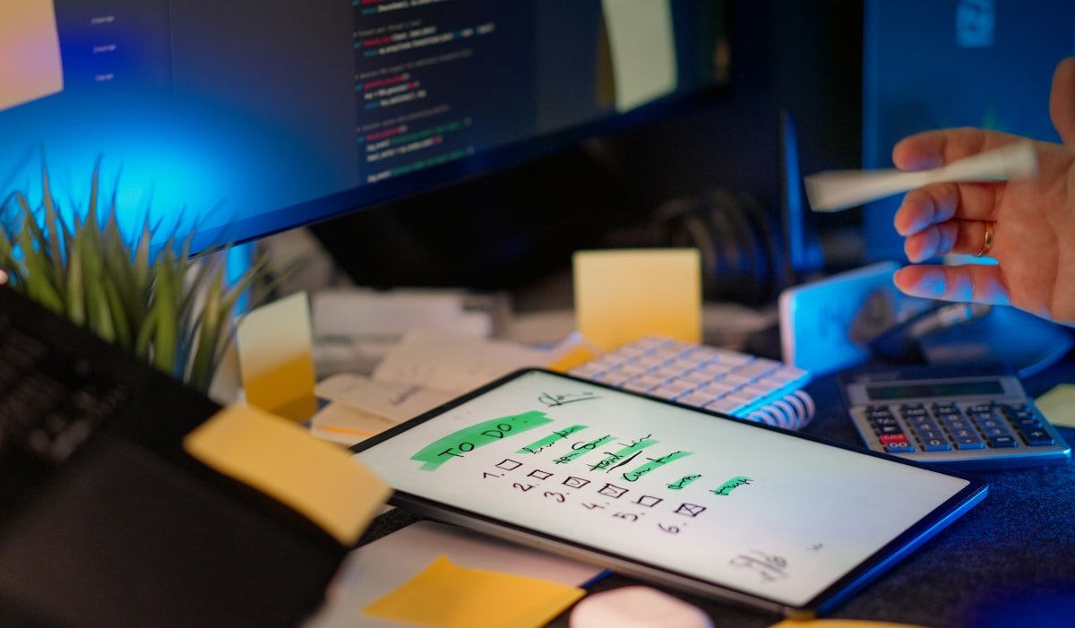 Developer workspace with code on monitors, to-do list, and sticky notes.