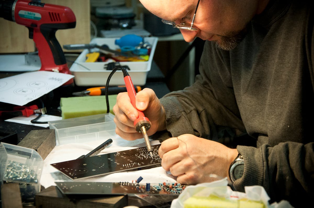 Technician soldering a circuit board at an electronics repair workbench.